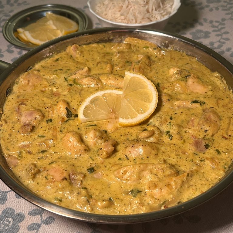 A stainless steel pan filled with bright yellow chicken curry on it, served with lemon slices and rice.