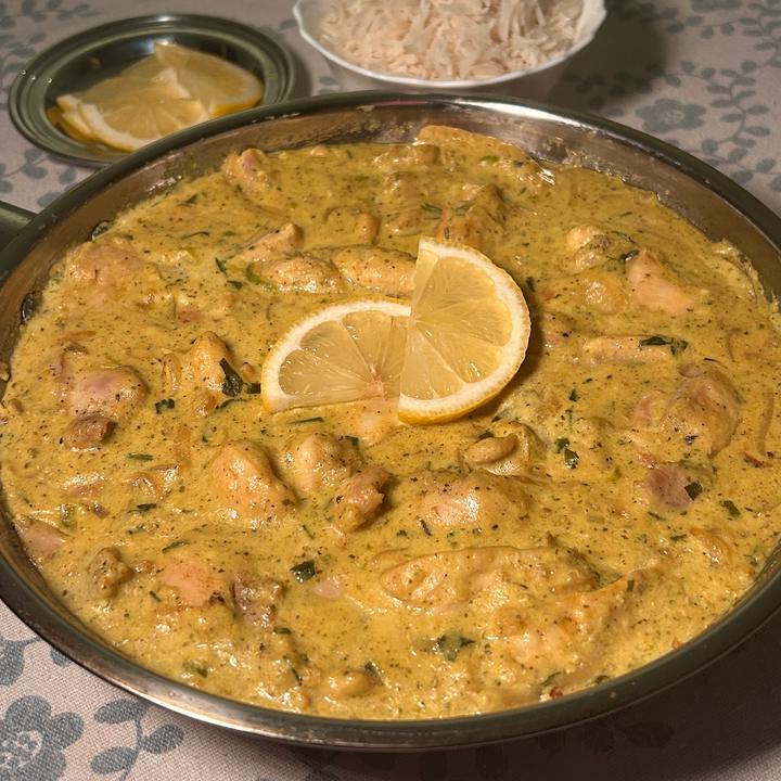A stainless steel pan filled with bright yellow chicken curry on it, served with lemon slices and rice.
