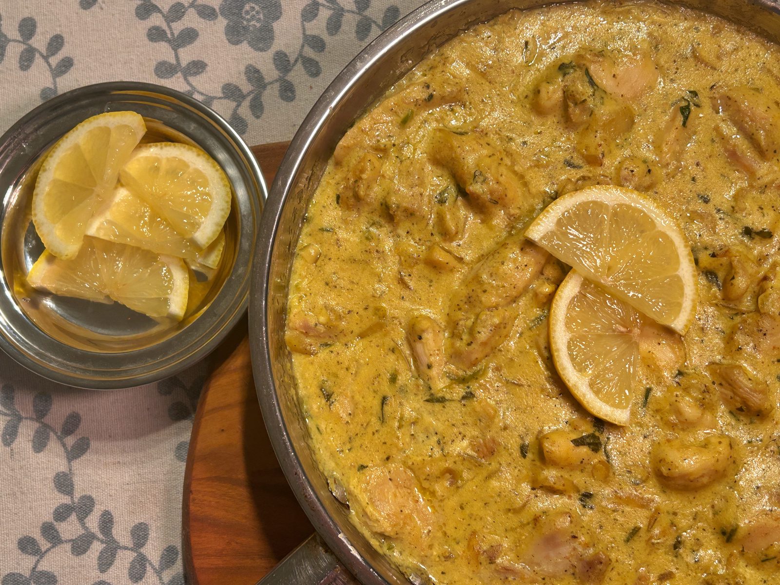 A stainless steel pan filled with bright yellow chicken curry on it, served with lemon slices and rice.