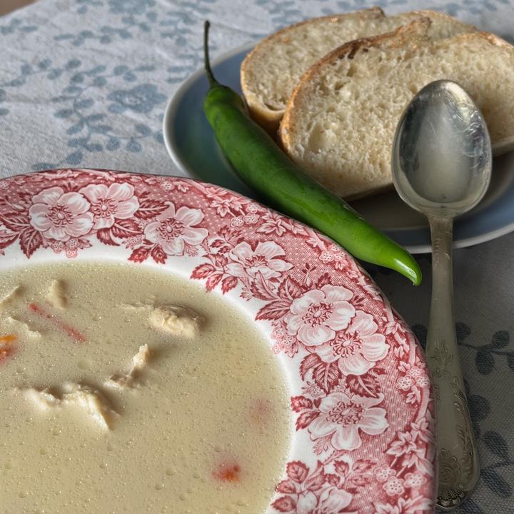 A bowl of soup, served with bread and a green chili pepper.
