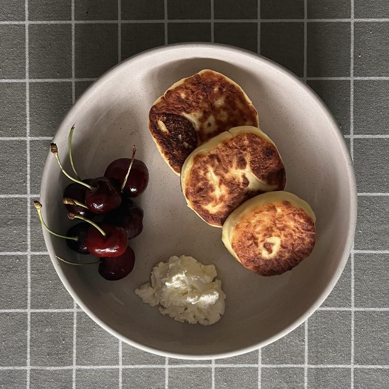 A bowl with three cottage cheese pancakes, served with cream cheese and sweet cherries