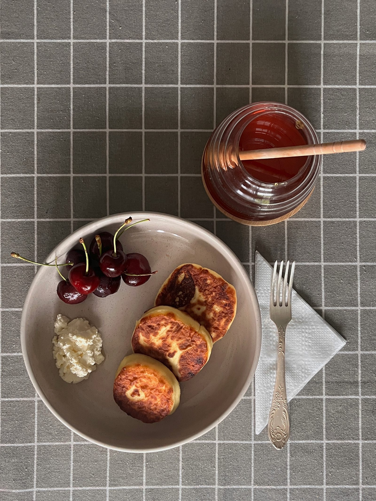 A bowl with three cottage cheese pancakes, served with cream cheese and sweet cherries